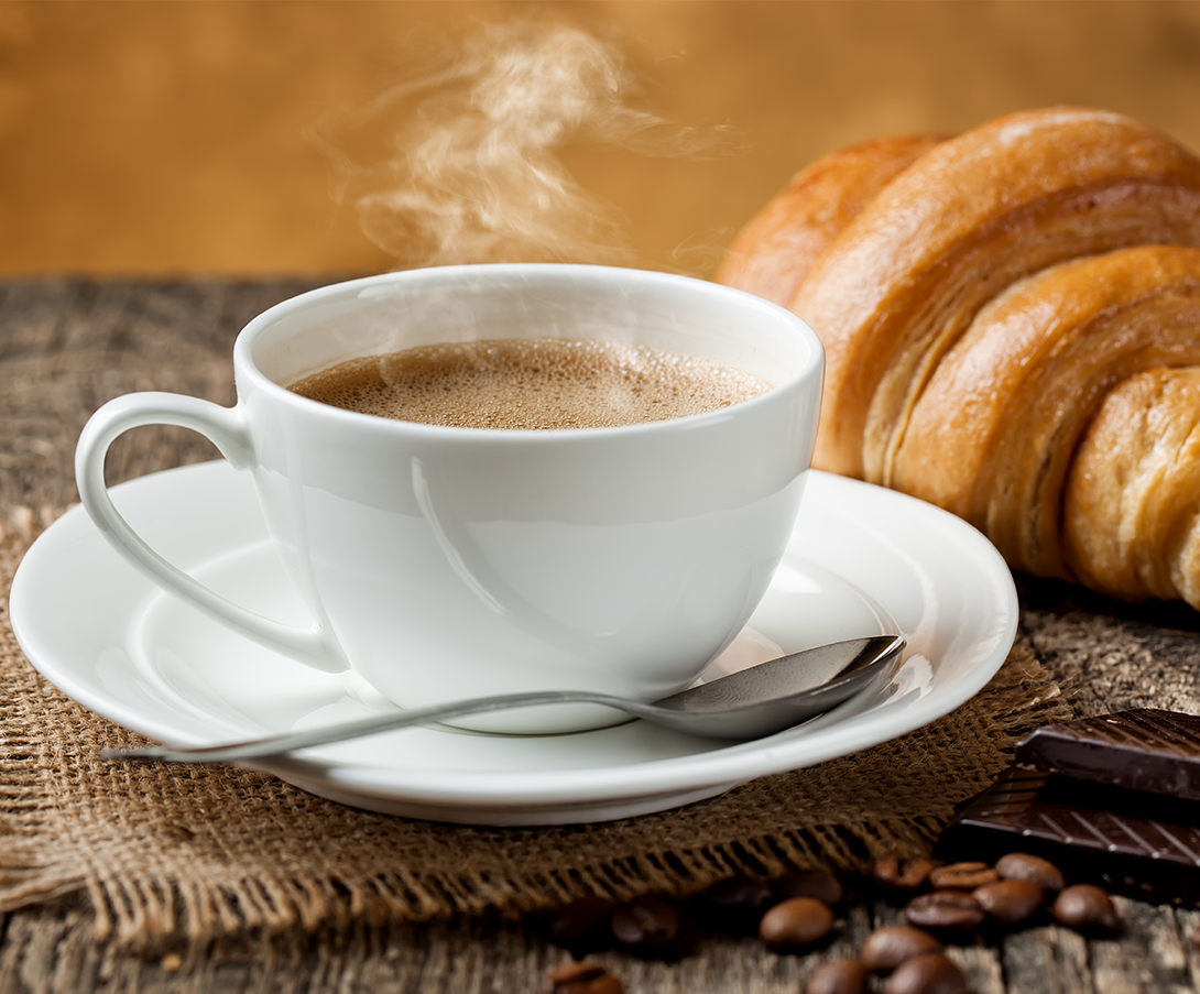 Dampfender Frühstückskaffee mit einem Crossaint im Hintergrund