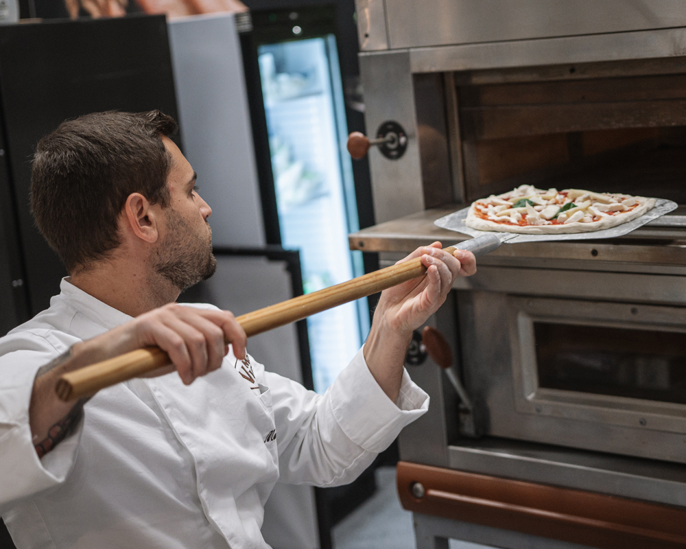 Pizzabäcker schiebt Pizza in den Ofen